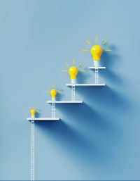 White ladders leaning on yellow lightbulbs to form a graph on over blue wall. Vertical composition with copy space. Creativity and solution concept.